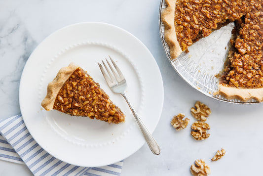 Whole maple walnut pie with a piece served on a plate.